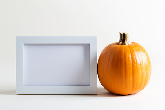 Blank white picture frame with a pumpkin on a white background