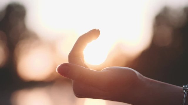 Sun in hands. Slow Motion 120 fps, 4K. Woman hand catching a sun against beautiful sunset on horizon. Nature. Vacation. Hope. Carpe diem. Opportunity concept. Freedom, hippie generation.