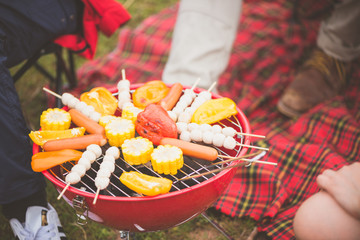 Group of man and woman enjoy camping picnic and barbecue at lake with tents in background. Young mixed race Asian woman and man. Vintage effect style pictures.