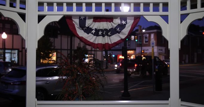 A nitghttime view of a small town street corner and traffic activity as seen through a gazebo.  	