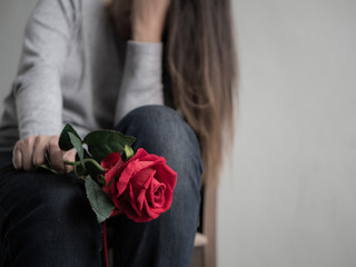 Sad woman sitting and crying with red rose in her hand. Lonly , love, emotion concept.
