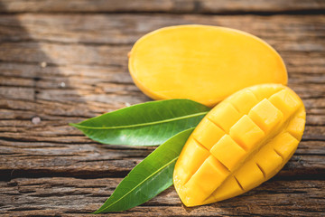 Sliced ripe mango on wooded board with green leaves.