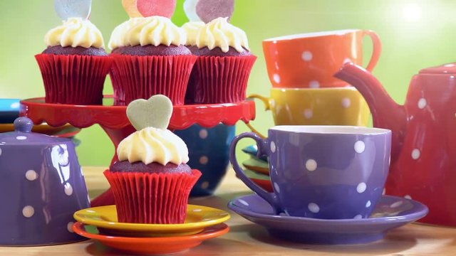 Colorful Mad Hatter style tea party with cupcakes and rainbow colored polka dot cups and saucers, with bokeh garden background and lens flare, panning up close up.