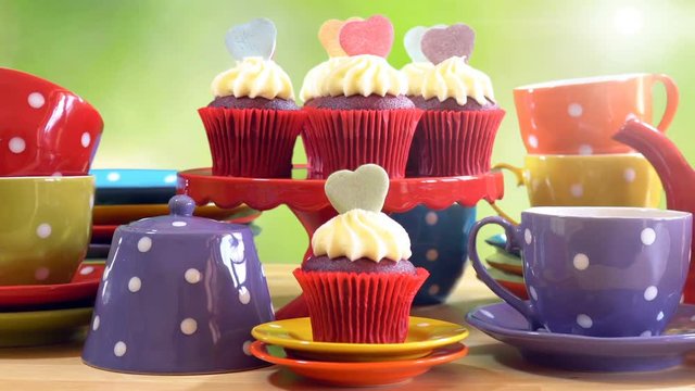 Colorful Mad Hatter style tea party with cupcakes and rainbow colored polka dot cups and saucers, with bokeh garden background and lens flare, panning across close up.