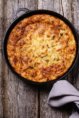 Zucchini, bacon and cheese casserole or gratin in cast-iron pan on vintage wooden table. Selective focus 