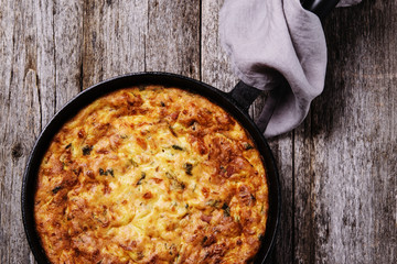 Zucchini, bacon and cheese casserole or gratin in cast-iron pan on vintage wooden table. Selective focus 