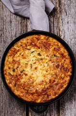 Zucchini, bacon and cheese casserole or gratin in cast-iron pan on vintage wooden table. Selective focus 