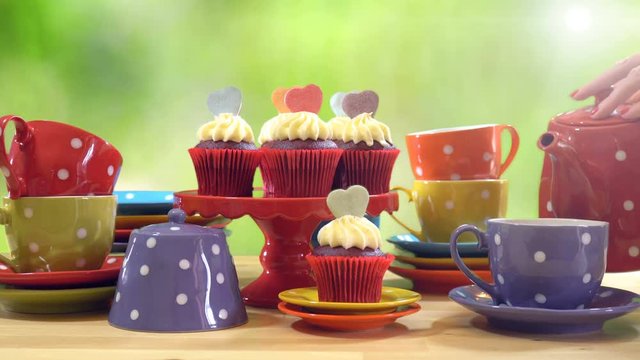 4k Colorful Mad Hatter style tea party with cupcakes and rainbow colored polka dot cups and saucers, with bokeh garden background and lens flare, pouring tea.