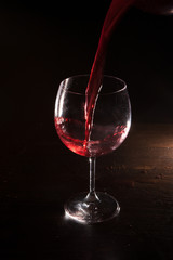 Red wine in motion on black background. Alcohol advertising closeup, exquisite beverage pouring in wine glass. Tasty alcoholic drink, commercial concept