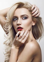Close-up beauty shot of a beautiful young blonde women with the wind in her hair and sensuality in the eyes. Gently touching her face.