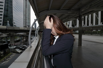 Low key portrait of stressed frustrated young Asian business woman touching head with hands and feeling tired or disappointment at urban city background.