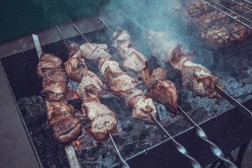 Grilled kebab cooking on metal skewers (grill). Roasted meat cooked at barbecue with smoke. Close up BBQ fresh pork meat chop slices. Traditional eastern dish, shish kebab.