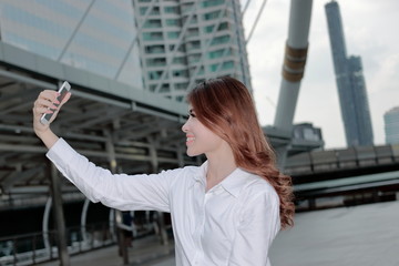 Fototapeta premium Side view of attractive young Asian woman taking a selfie photo at urban city background.
