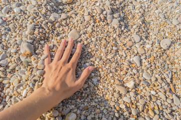 Female hand touches little pebbles on a sea beach