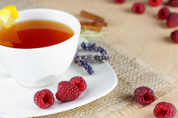 Mug of fruit tea and raspberries on cloth on the table