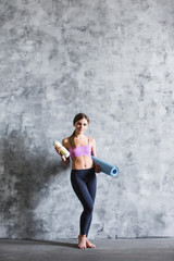 Young beautiful woman after workout with a bottle and yoga mat.