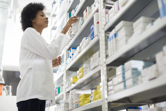 Female Chemist Arranging Stock In Shelves At Pharmacy