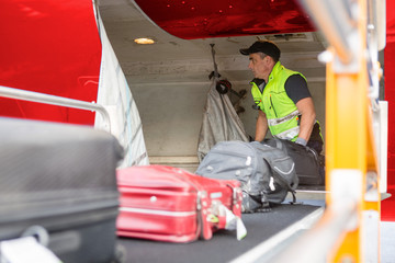 Fototapeta premium Worker Placing Luggage On Conveyor To Unload Airplane