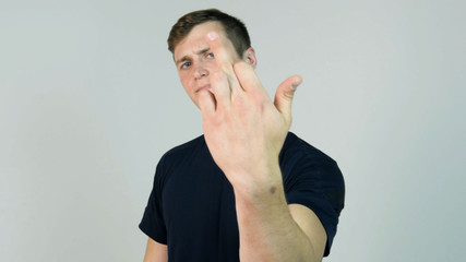 Young Man Showing Middle Finger Isolated on White. Young angry man with black t-shirt looking at...