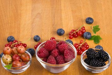 on a wooden board three plates of berries, as a background