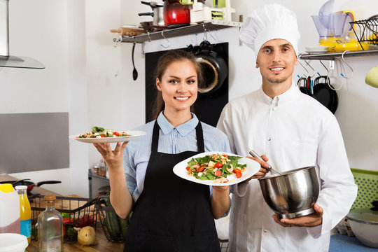 Smiling cook giving to waitress ready to serve salad