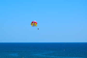 Tourists fly over the sea on a parachute behind a boat (Paraseyling).