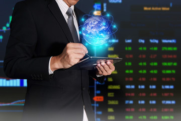 Businessman working with tablet for trading (sell/buy) the Stock Exchange and glowing networking world map  as business, communication and investment concept. Elements of this image furnished by NASA