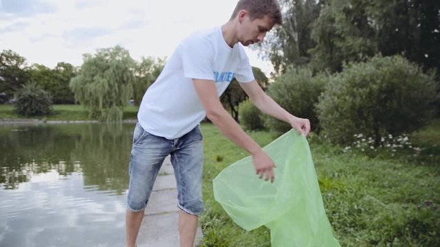 Young man volunteer pulls a plastic bottle from a pond and throw in garbage bag