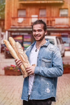 Junger Mann mit mehreren Stangen frischen Baguette im Arm auf der Strasse.