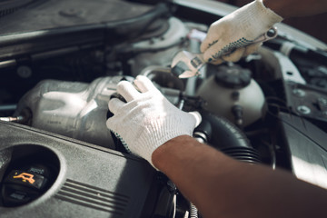 Close-up. A man is fixing a car with a wrench. White car. White gloves for repair