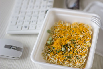 Chinese noodles on the desktop next to the keyboard. Eating instant noodles on work desk. food is on the desktop