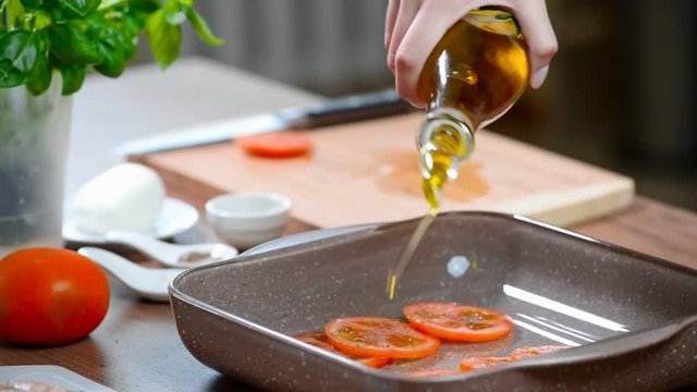 Pouring olive oil over tomato. Cooking the chicken Caprese