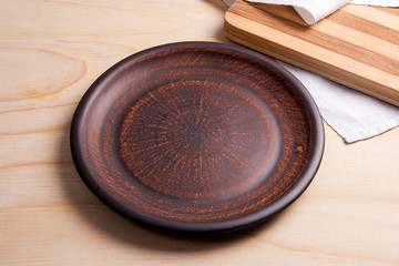 Empty brown clay plate and cutting board on wooden background.