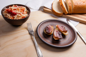 Baked potatoes with slices of bacon and eating utensils on wooden background. Sauerkraut in clay bowl and slices of white bread on cutting board..