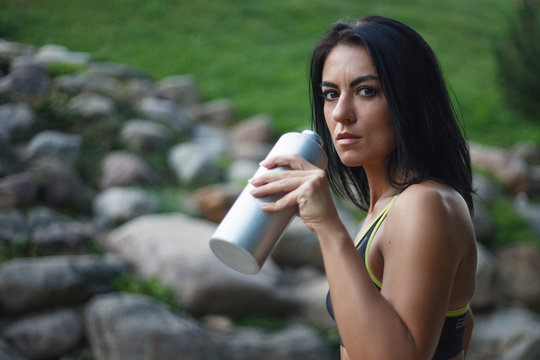 View side of fitness wonan with black hair holding a water bottle on the park background