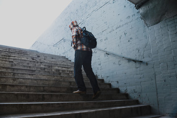 Hipster in a checkered shirt rises the stairs from the underpass