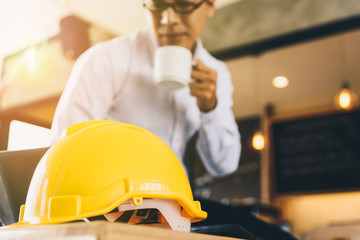 Yellow hard safety helmet hat for safety project of workman as engineer or worke On a wooden desk.Architect is the background blurred.