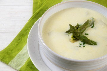white asparagus cream soup with green asparagus heads garnish in a bowl, green napkin, white table, closeup with selected focus and narrow depth of field