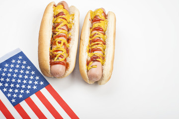 Two hotdogs with ketchup and mustard next to American flag on white background. Isolated. Fastfood.