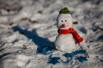 Snowman on snow over blurred christmas tree and gift box on glitter light bokeh background with copy space
