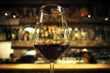glass of red wine, drink with blurred bottles of alcohol on background (warm tone)