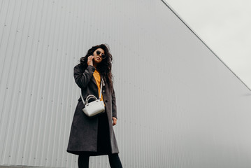 Portrait of stylish modern young curly woman in coat sunglasses
