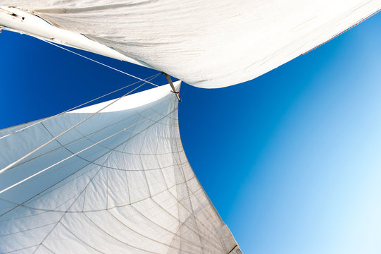 White yacht sails in sunlight on blue cloudy sky background.