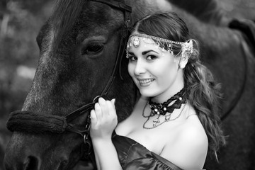 Beautiful girl near big black horse, pinto with a spot, long dress and expensive jewelry. Forest,...