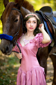 Beautiful girl near brown horse, pinto with a spot, blue decorations on horse, pink dress an jewelry. Forest, soft light, professional photo. Looks like film or fairy tail, cosplay