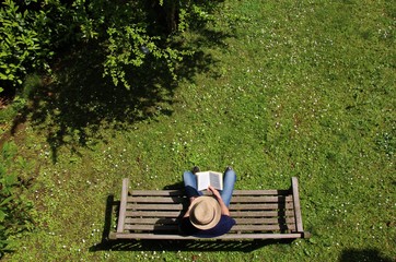 Boy with straw hat reading a book on a wooden bench