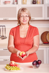 Woman preparing fruit in the kitchen. Adult woman holding fresh fruit. Happy woman holding plate full of fruits in the kitchen background. Apples, plums, grapes - kitchen stories are preparing food.