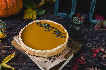 pumpkin pie on wooden board with autumn leaves, green wooden box, fresh pumpkin, pumpkin seeds, anise on brown wooden table, toned for a vintage effect