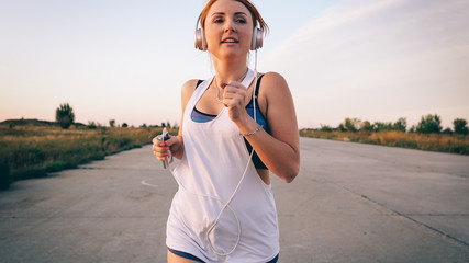 young woman runs and listens to music on headphones on a summer afternoon at sunset