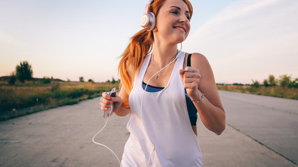 young woman runs and listens to music on headphones on a summer afternoon at sunset